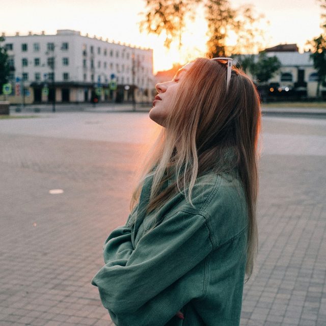 Женщина подставляет лицо закатному солнцу на городской улице