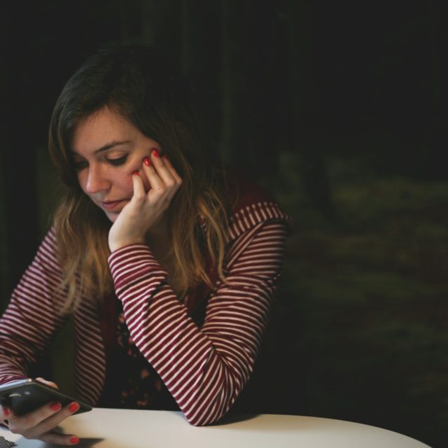 Женщина за столом смотрит в телефон, приглушённый кинематографичный свет