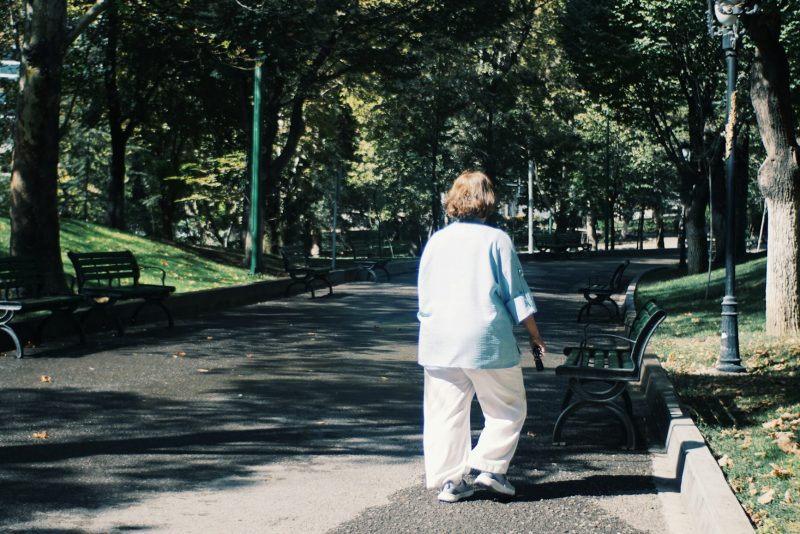 Женщина уходит вглубь парковой аллеи вдоль деревьев