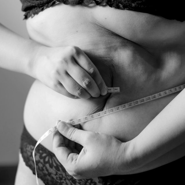 A person in black lace underwear measuring their waist with a white tape measure
