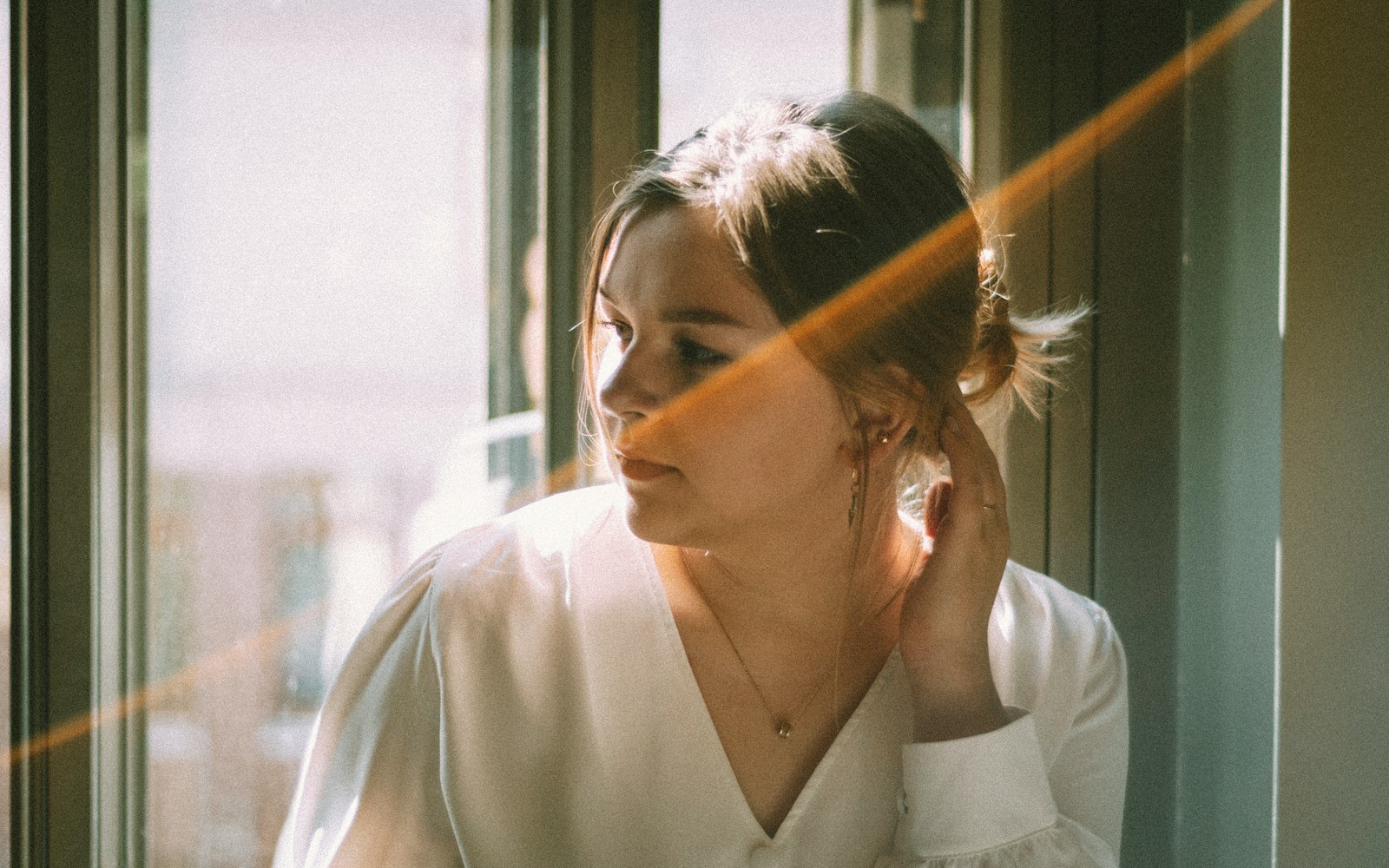 a woman looking out of a window while wearing a white shirt