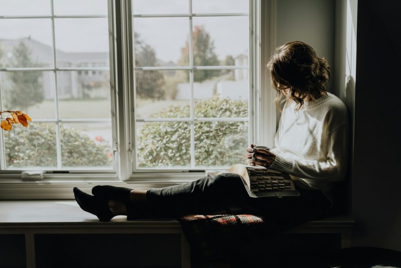 A woman sitting on a window sill reading a book
