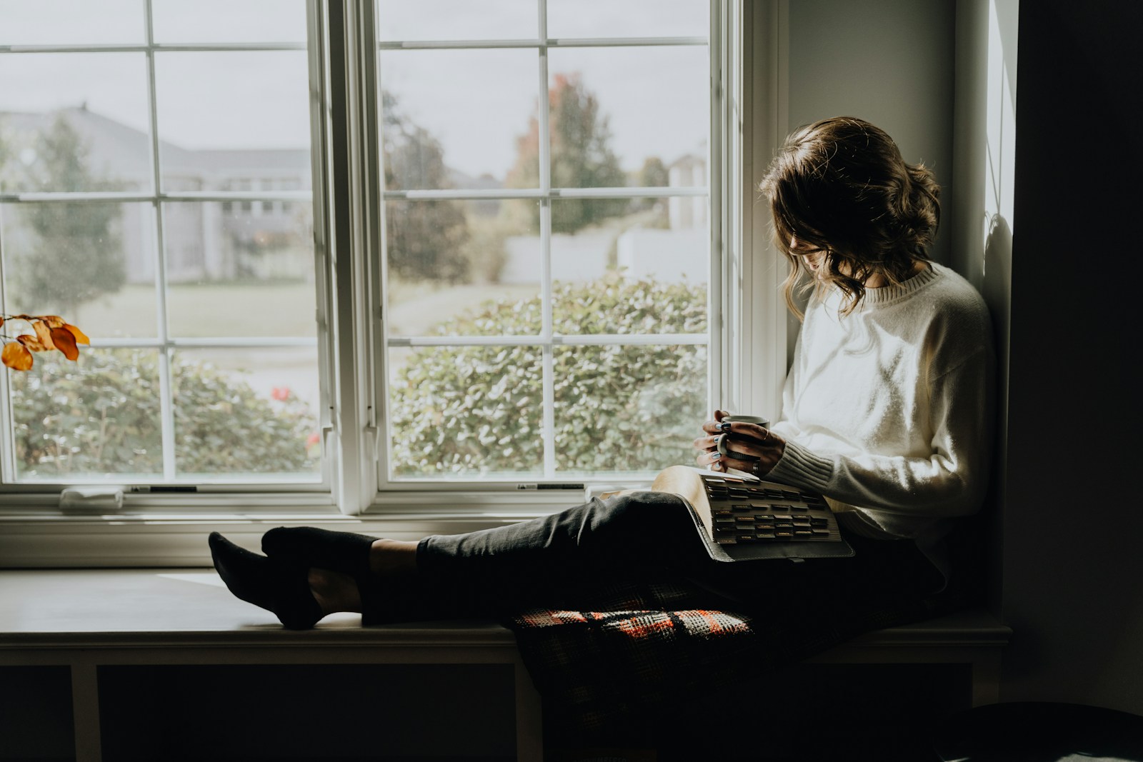 A woman sitting on a window sill reading a book
