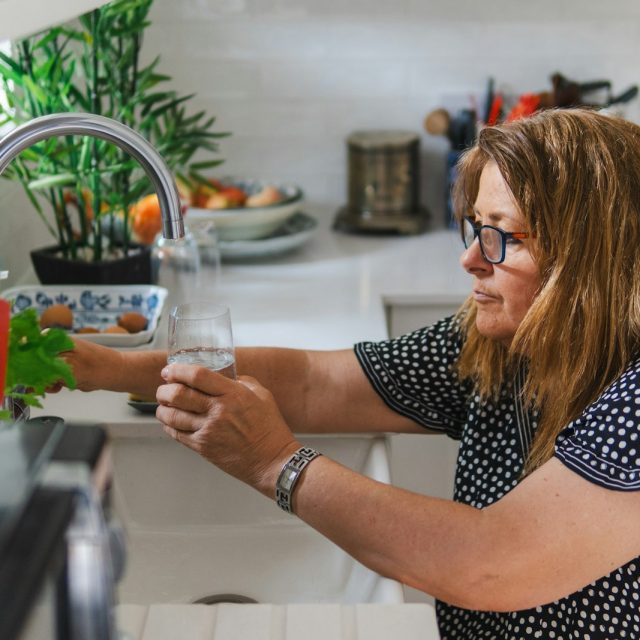 Woman filling a glass with water from a kitchen faucet